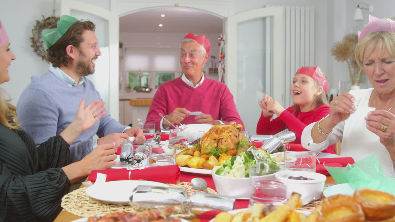 크리스마스 크래커에서 선물로 종이 모자를 입은 가족들이 함께 식사하는 테이블에 앉아 있습니다.