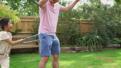 Asian-Father-And-Daughter-Having-Fun-Playing-With-Hula-Hoop-In-Garden-At-Home