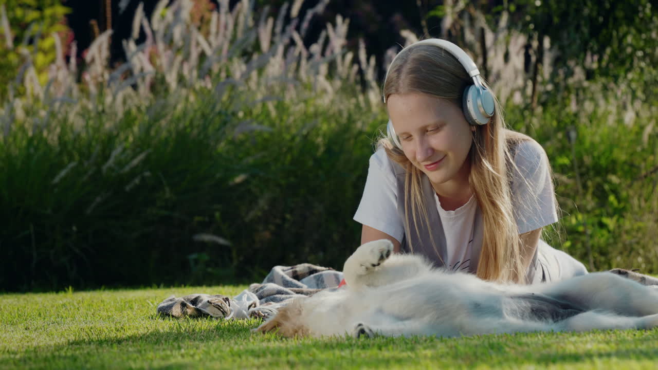 십대 소녀는 강아지와 함께 놀고, 잔디에 누워서 헤드폰으로 음악을 듣습니다.