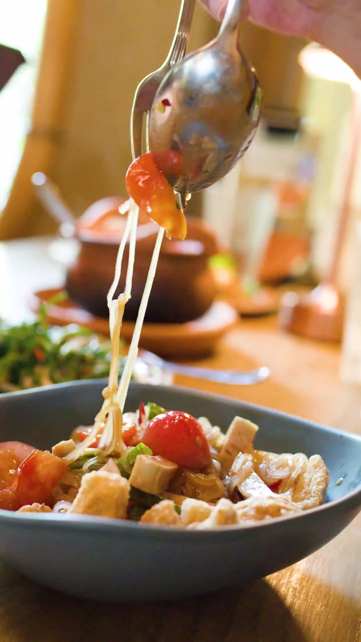 Una mano mescola un'insalata piccante di vermicelli di riso thailandesi con luce naturale, primo piano, ambientazione da ristorante, ripresa a mano.