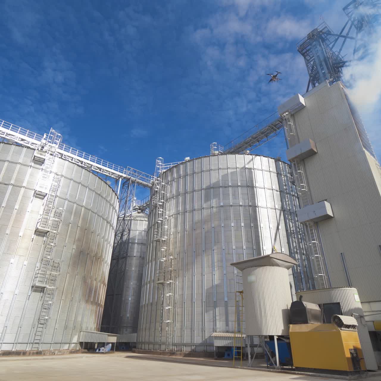 Panoramic view of agricultural plant. Large round grain elevators for storing grains. Thick fumes releasing into the air during grain processing on a factory