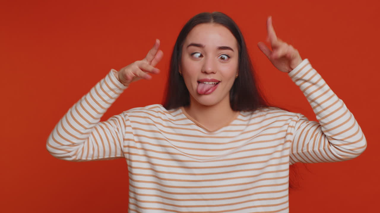 재미있고 즐거운 여자가 장난스럽고 어리석은 표정을 짓고, 찡그린 표정을 짓고, 혀를 보여주는 장난을 칩니다.