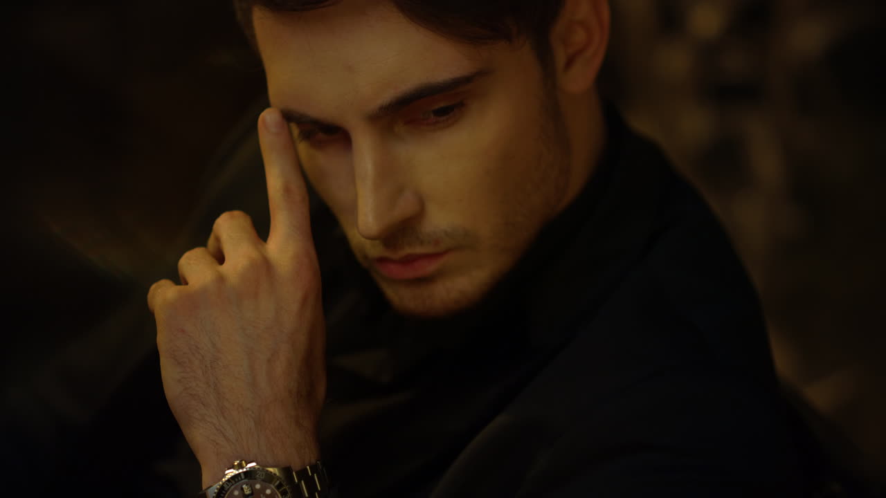 어두운 배경에서 멀리 보이는 집중된 남자. 부자가 실내에서 얼굴을 만지고 있다.