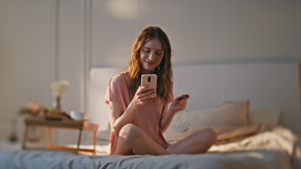 웃는 여자가 빛 침실에서 지불을 하고 있습니다. 휴식하는 소녀 주말을 유지합니다.