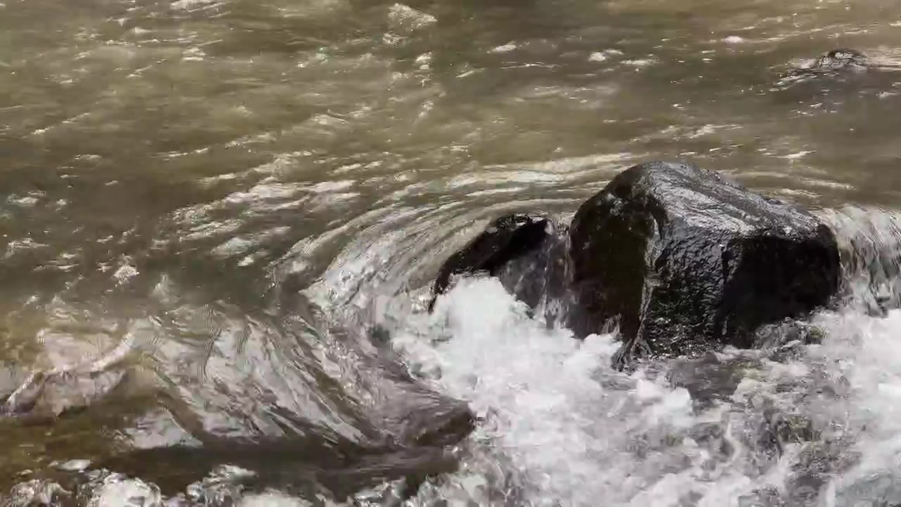 Acqua che scorre attorno a una roccia scura in un fiume.
