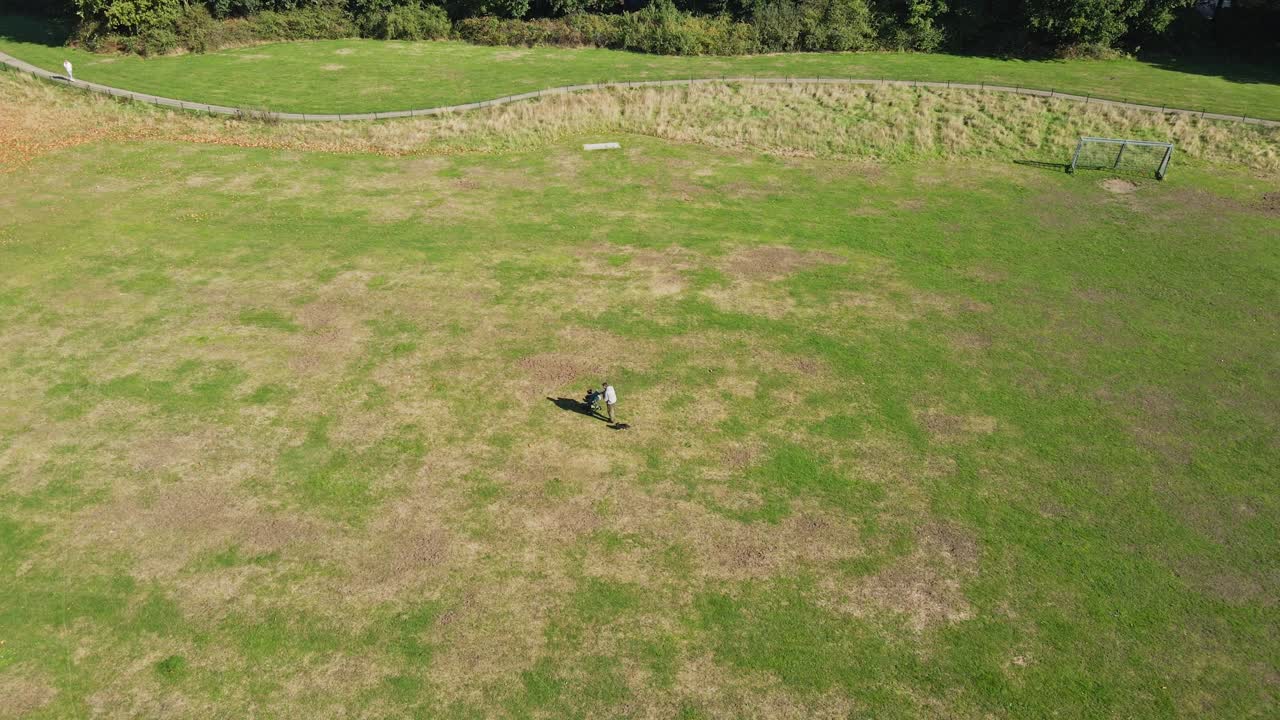 마른 풀이 있는 공원을 가로질러 유모차와 작은 개와 함께 걷는 남자의 지브 다운