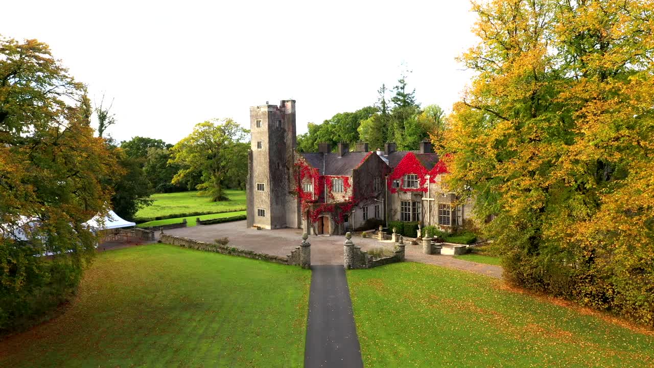 Slow reveal of Belle Isle Castle from entrance path lined with rich golden autumn foliage, approach to building