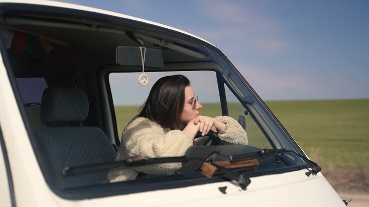 Una bella ragazza con occhiali da sole al volante di una roulotte ferma su una strada isolata in mezzo alla campagna.