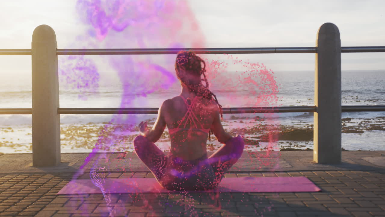animación de manchas coloridas sobre una mujer biracial meditando junto al mar