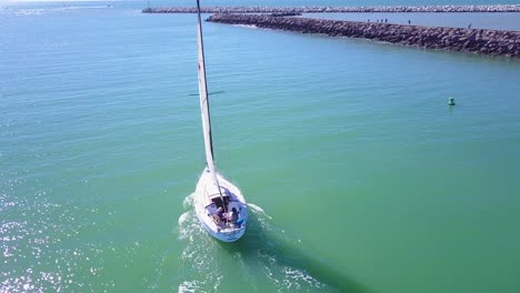 Good-aerial-above-a-small-sailboat-heading-out-of-a-harbor