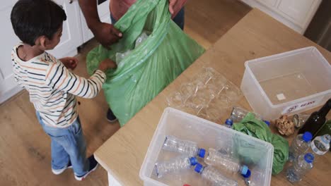 high angle view of happy biracial father and son segregating waste in kitchen, slow motion