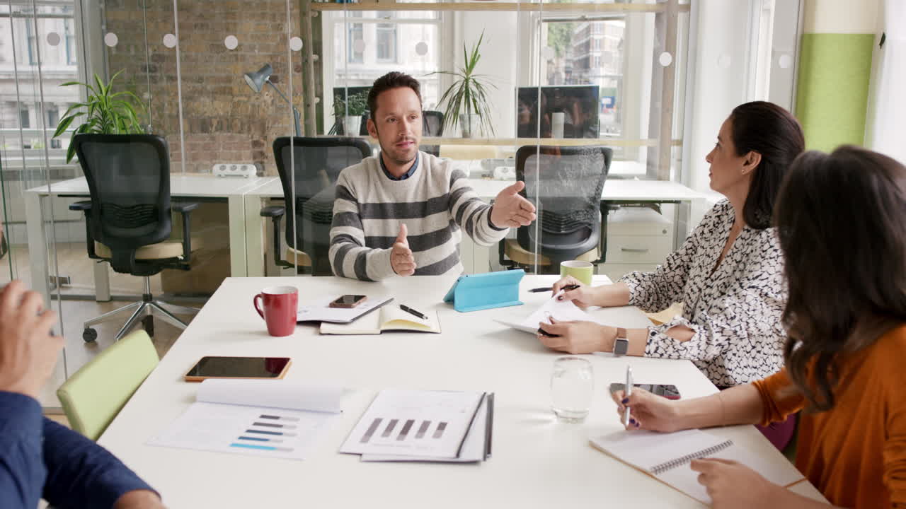 Creative Business team meeting businessman manager presenting financial data to shareholders using digital tablet in casual modern office boardroom with natural light and large open windows
