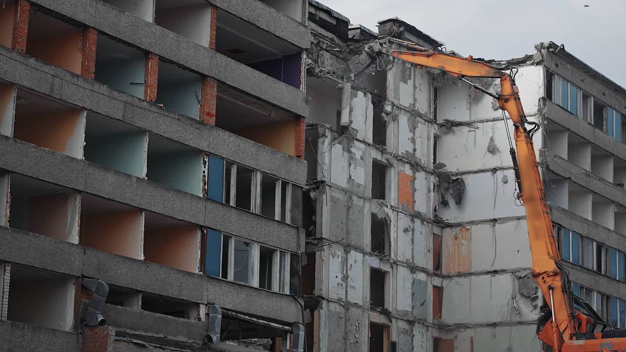 Excavator claw tearing off the big block in the condemned building. Heavy cement block falling down with clouds of dust. Demolition machinery work.