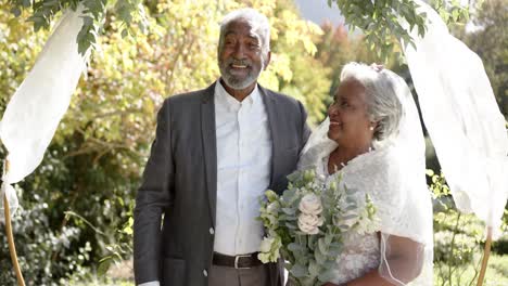 Portrait-of-happy-senior-biracial-couple-embracing-during-wedding-ceremony-in-garden,-slow-motion