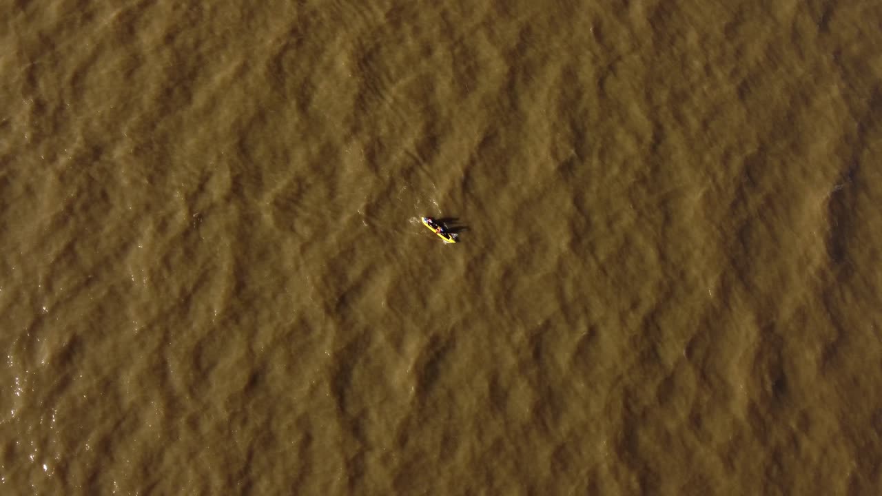 Aerial top down shot of two rowers in yellow kayak paddling on brown colored River Plate near Buenos Aires during sunset