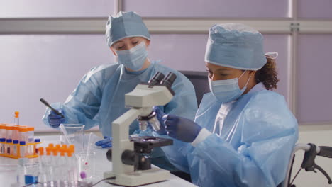 trabajadora de laboratorio en silla de ruedas con ppe analizando muestras en el laboratorio con microscopio