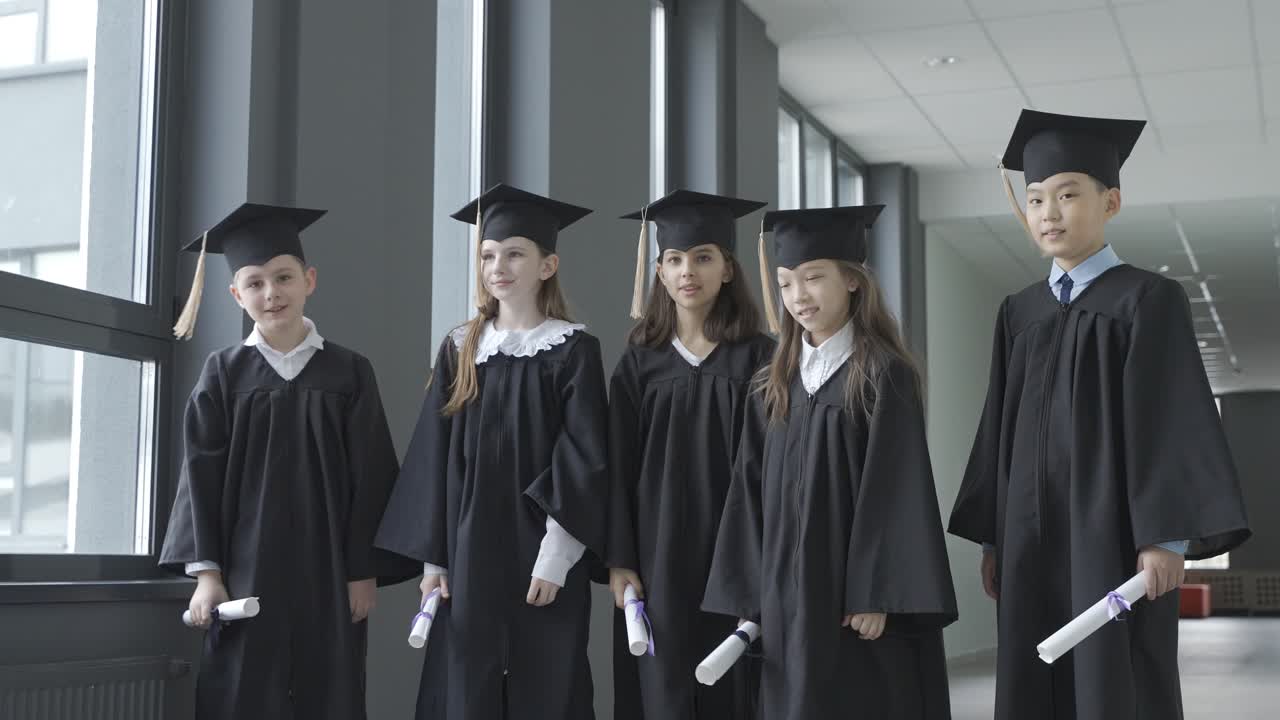 группа счастливых многорасовых студентов дошкольного отделения в ступах и мантиях. они держат дипломы и машут руками.