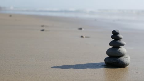 rock balancing on ocean beach, stones stacking by sea water waves. pyramid of pebbles on sandy shore