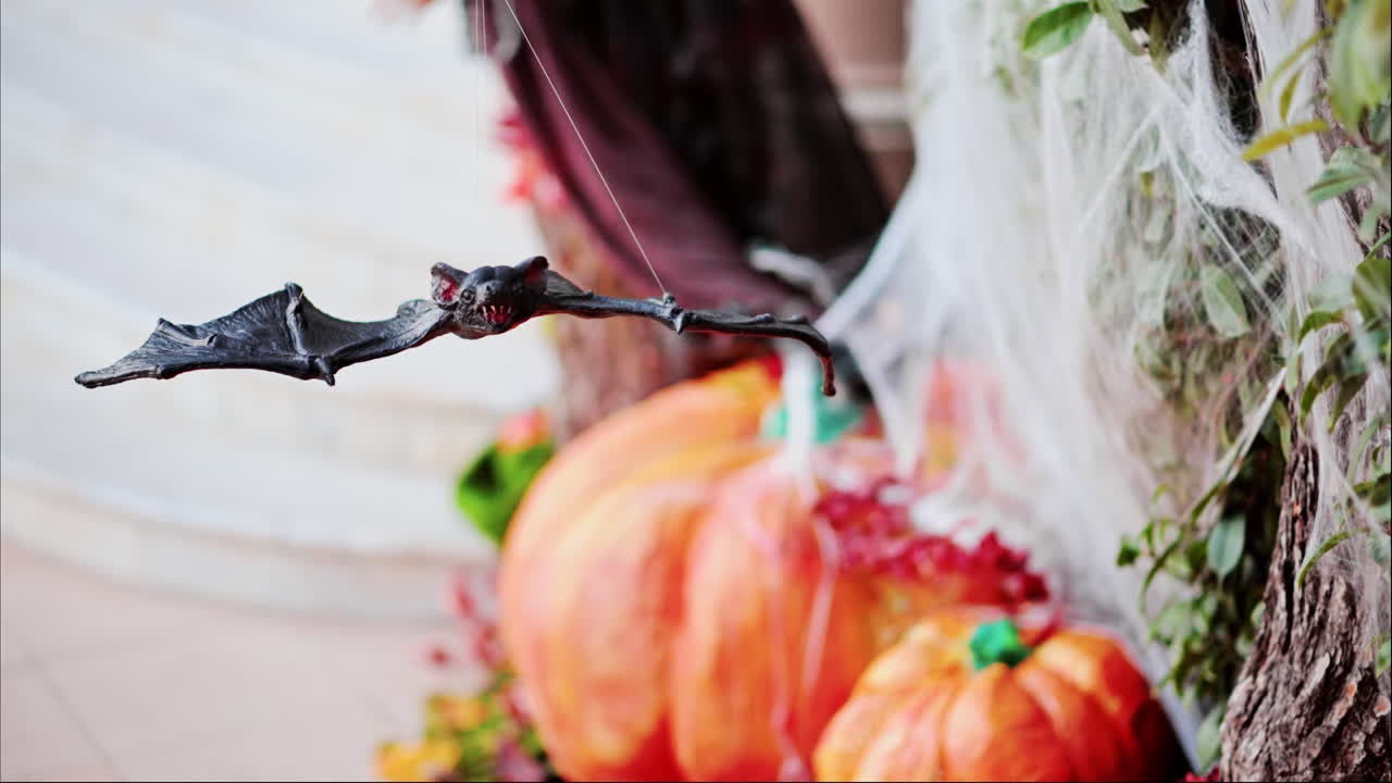 A bat figurine suspended above halloween decorations of pumpkins and spider webs