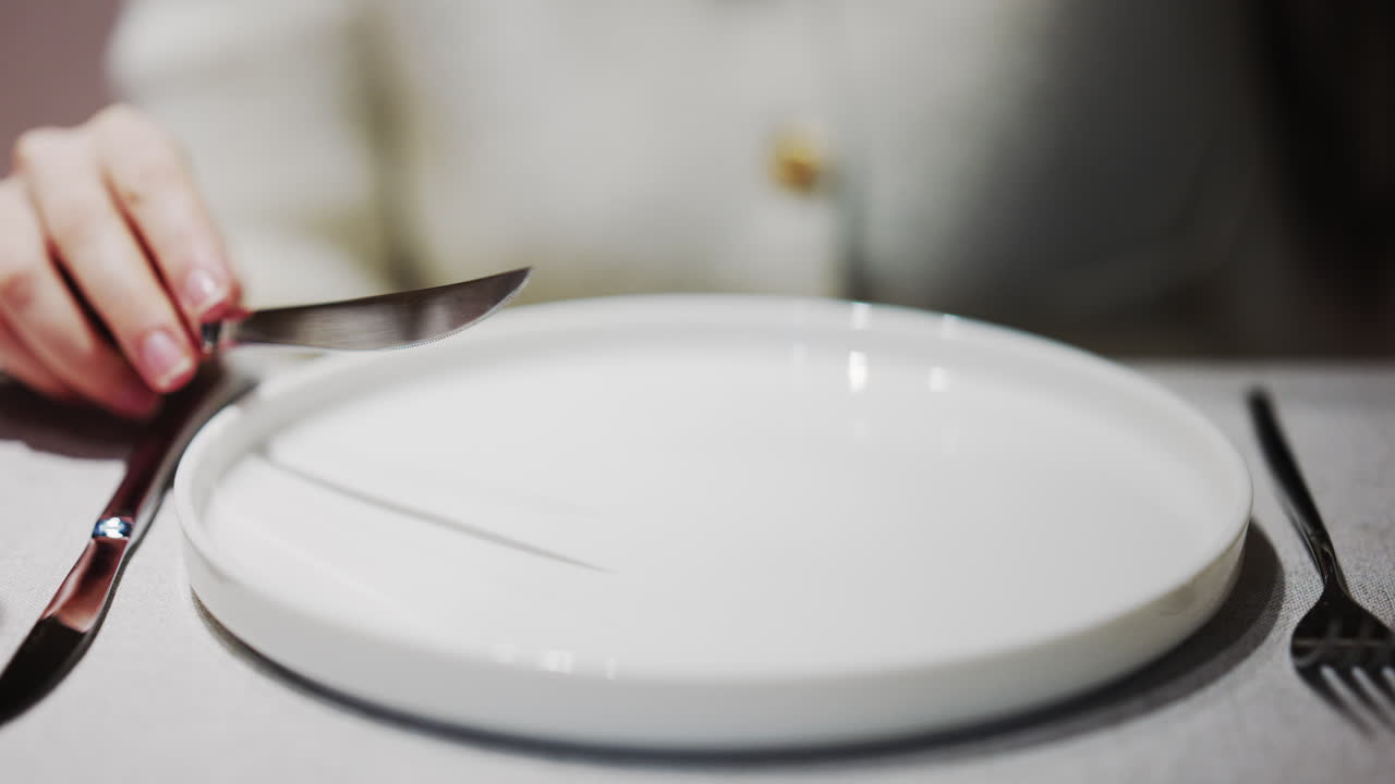 Primo piano di mani che tengono forchetta e coltello sopra un piatto bianco vuoto in un'ambientazione da ristorante
