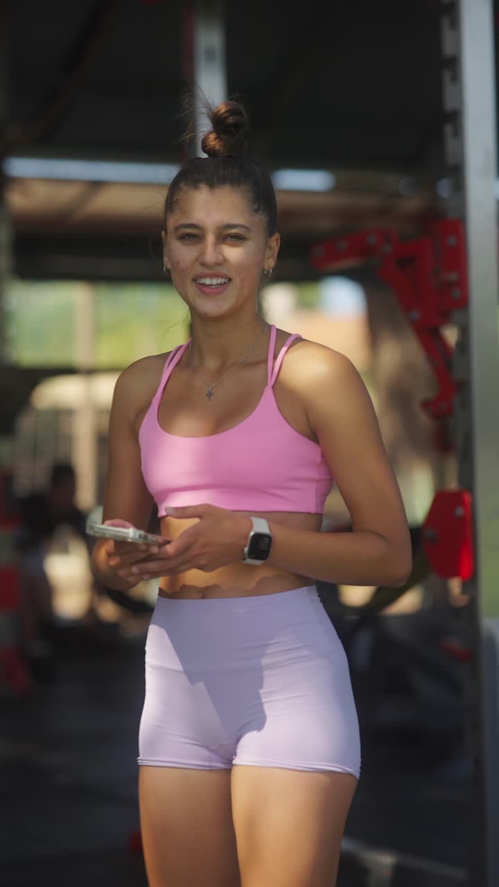 Young woman in activewear at an outdoor gym with a smartphone