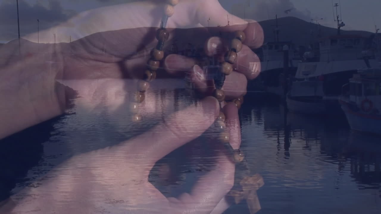 Holding wooden beads, hands overlooking serene harbor with boats at dusk animation