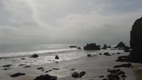 Drone-flyover-El-Matador-beach,-rock-formations-on-Cloudy-morning,-Malibu