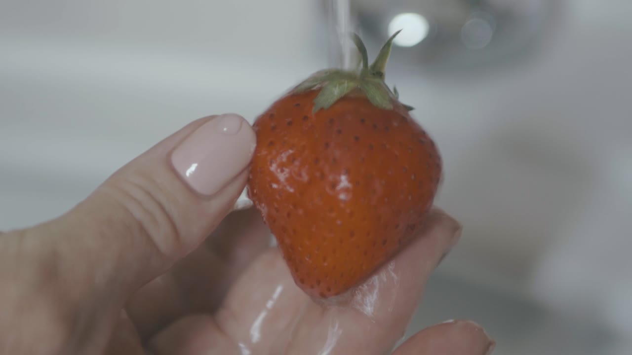 el agua fluye a cámara lenta sobre una fresa roja muy sabrosa, fondo blanco limpio