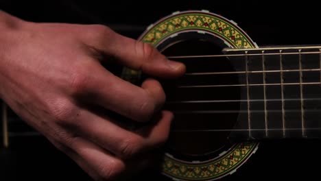 captura de detalle de la mano derecha del guitarrista rasgueando las cuerdas de una guitarra