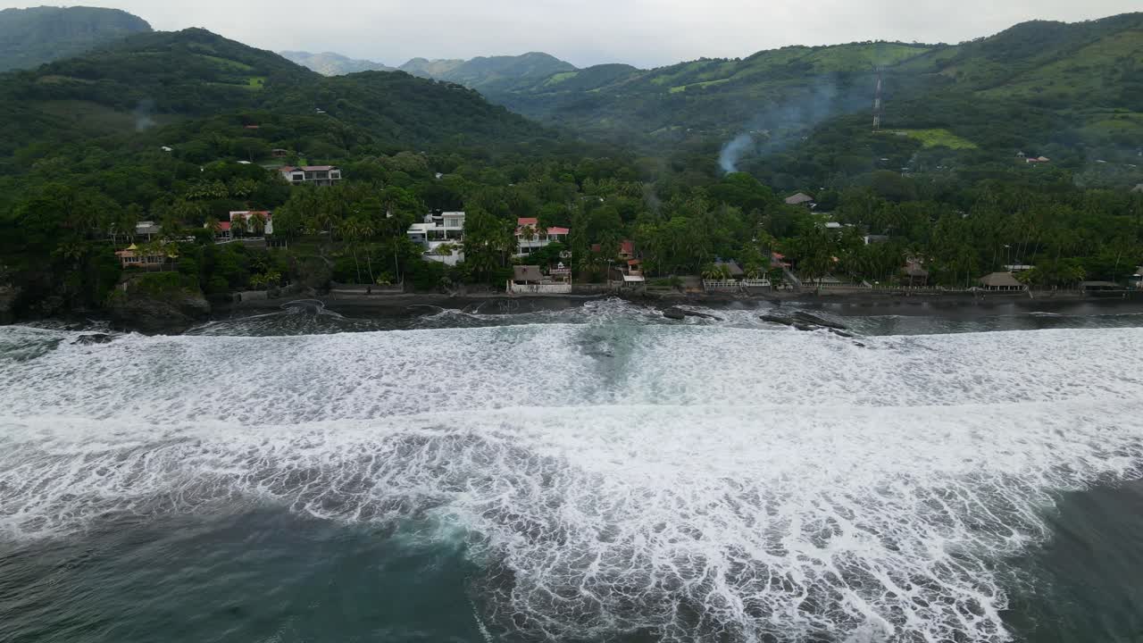 Aerial view moving left shot, scenic view of houses on the shoreline of the bitcoin beach in El Salvador Mexico, mountain ranges in the background