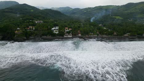 Aerial-view-moving-left-shot,-scenic-view-of-houses-on-the-shoreline-of-the-bitcoin-beach-in-El-Salvador-Mexico,-mountain-ranges-in-the-background