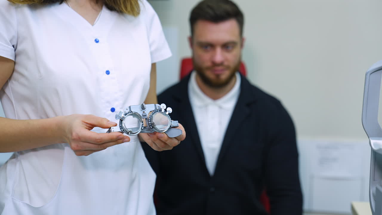 Testing glasses in doctor's hands. Ophthalmologist in medical gown standing near the patient and holding trial frame glasses in clinic. Eyesight concept.