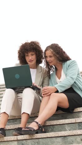 businesswomen celebrating success using laptop on stairs. vertical