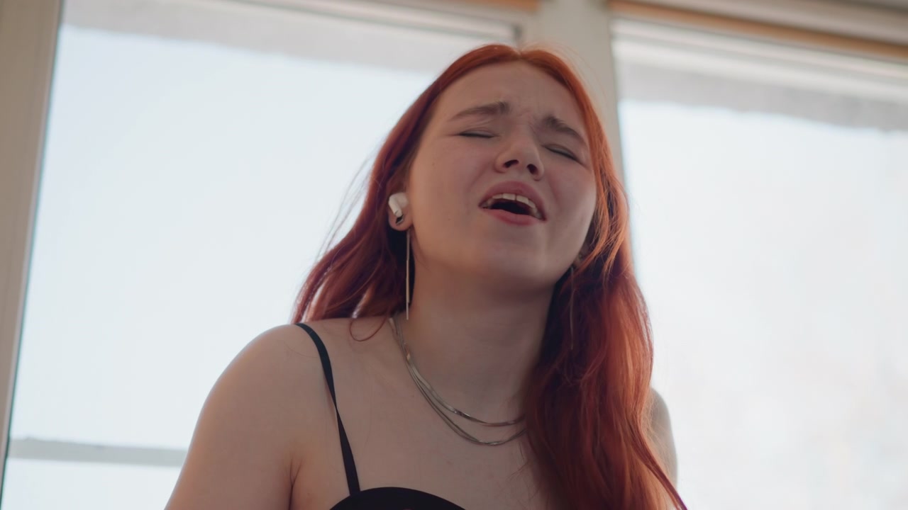 Artista vocale che trasmette sentimenti profondi attraverso un'illuminazione e una scena drammatiche. Cantante espressiva che evoca emozioni potenti mentre è illuminata drammaticamente contro uno sfondo di finestra luminosa.