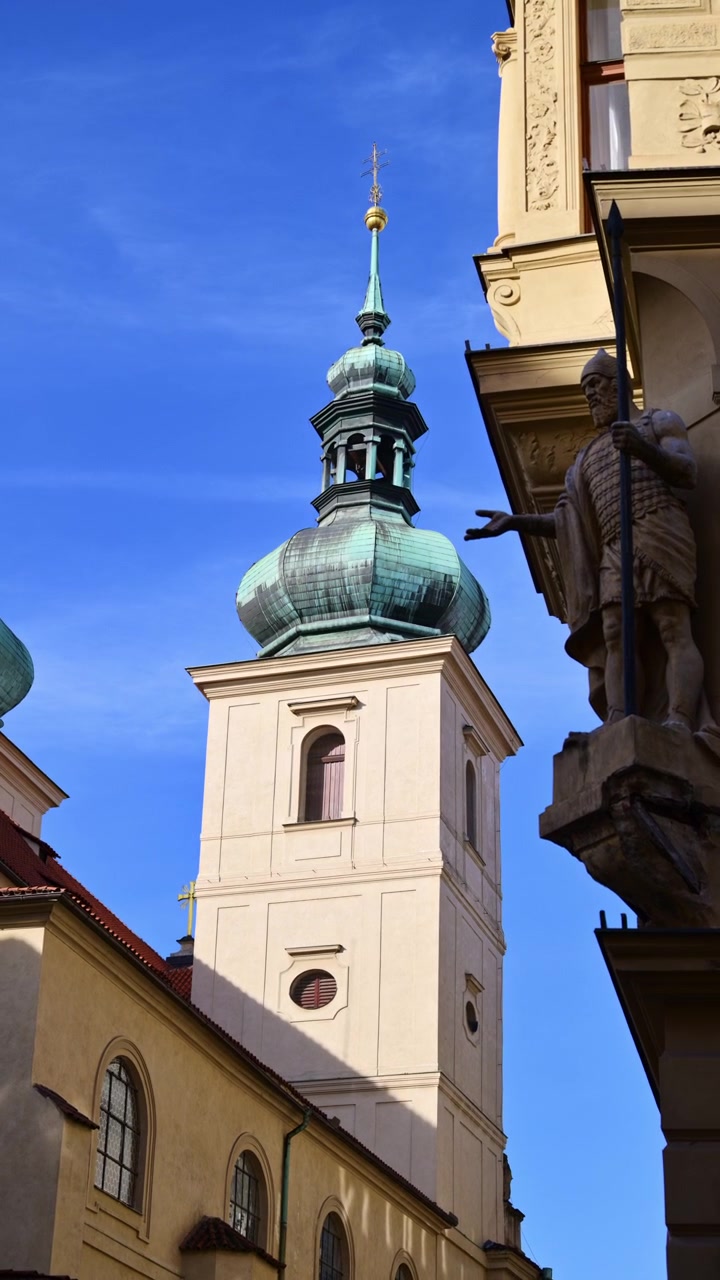 Vista verticale di una torre campanaria barocca con una cupola a cipolla verde sopra una stretta strada del centro storico, Praga, Repubblica Ceca