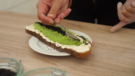 preparando aguacate sobre pan tostado con semillas de sésamo blanco y negro y hummus