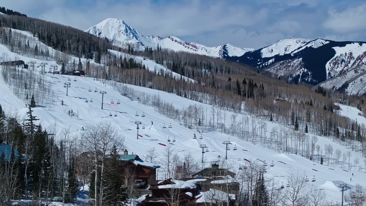 Powdery snow blankets slope with skier carving through deep turns under soft afternoon light, Snowmass Colorado USA aerial reveal
