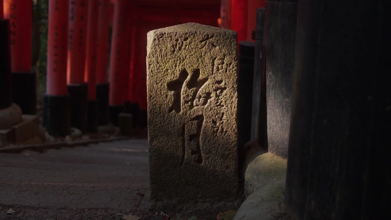 Stele di pietra al santuario Fushimi Inari a Kyoto con cancelli torii rossi sullo sfondo. Luce calda e atmosfera tradizionale giapponese.