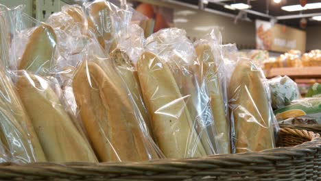 close-up of many packaged baguettes in a big wicker basket and a male customer takes one