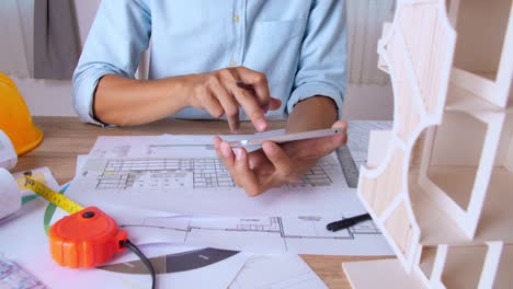 architect working a building blueprint and tablet with architectural house model