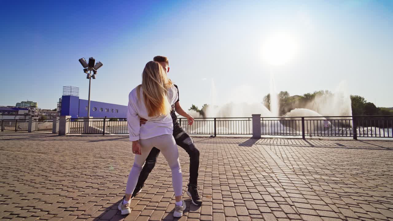 Modern dancers are dancing in the street. Urban lifestyle. Hip-hop generation. Boy's and girl's emotional moves on the video. Paving stones and young dacing couple at fontain background.