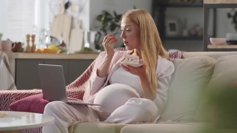 pregnant woman eating cake and watching movie on laptop