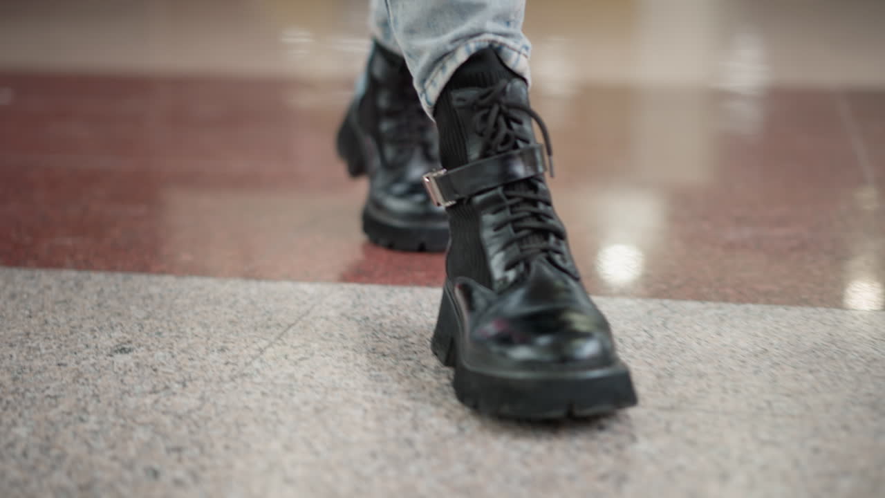 leg view of woman in chunky black boots pacing across polished mall floor then pausing midstride beside moving walkway bench detail captures stylish footwear motion stop moment