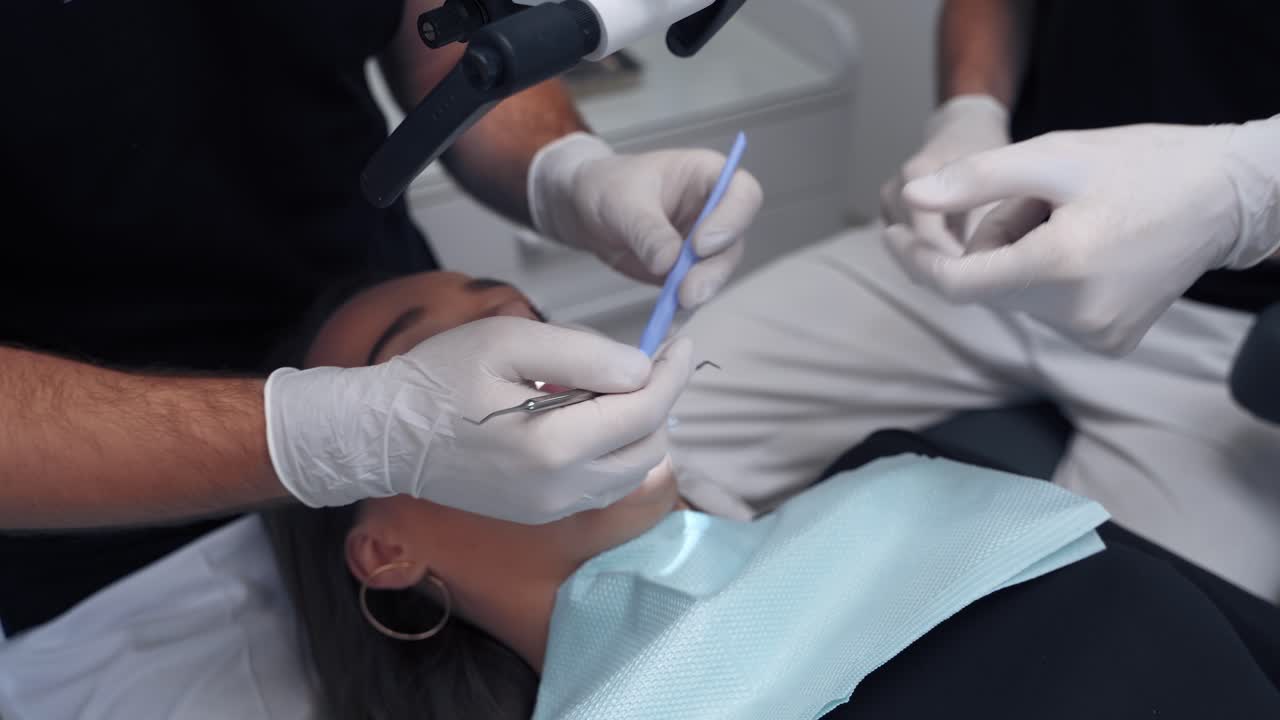 Dentist with assistant treating female's teeth. Medical tools in doctors hands during patient's teeth check up. Woman visits stomatologist. Close-up.