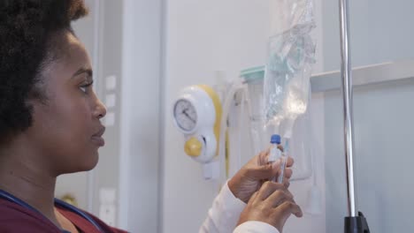 african american female doctor checking drip in hospital room, slow motion