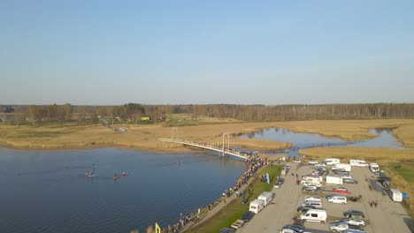 aerial view of võhandu rowing marathon along the river. crowd, spectators have gathered on the bridge and shore sidewalk to watch race on water while canoes, kayaks, paddleboards rowing and paddling