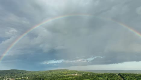 a right panning aerial view of a rainbow after a thunderstorm over the beautiful green countryside