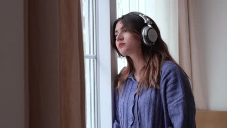 young girl watching out the window while listening to a sad song