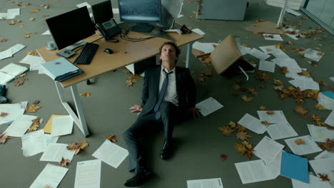 man lying amidst chaos in a leaf-strewn office