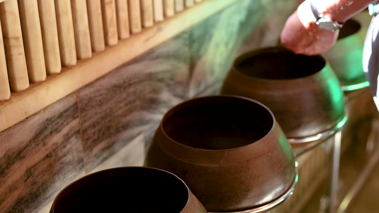 A person places coins into alms bowls at Wat Pho, Bangkok. The serene environment is highlighted by soft lighting and traditional decor